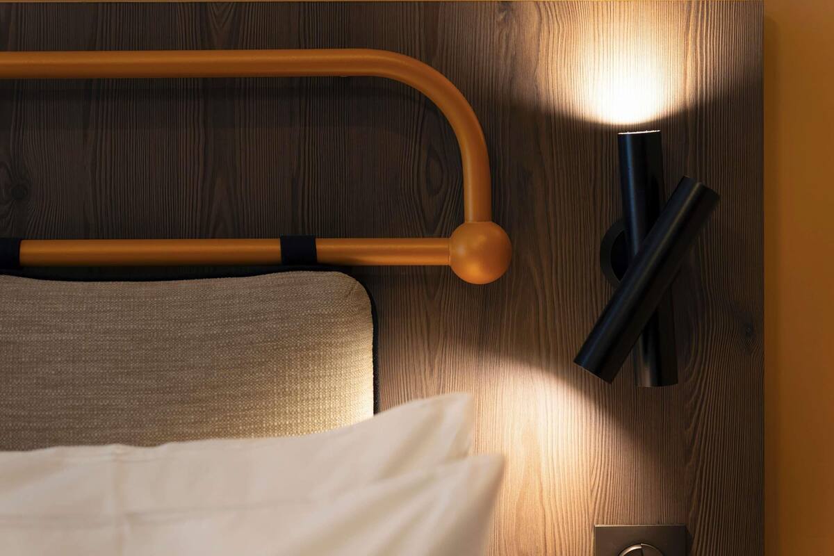 A bed with a headboard, a bedside table, and a wall-mounted light fixture.