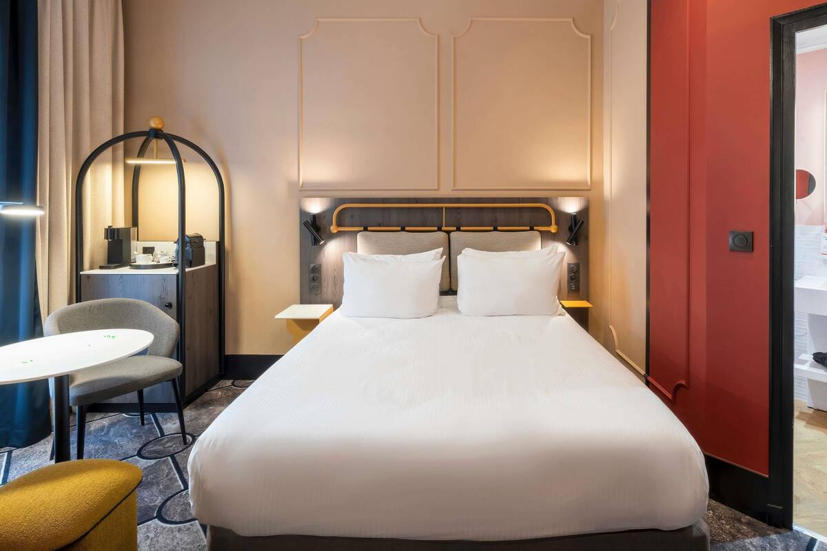Una habitación de hotel con cama, escritorio, silla y espejo.