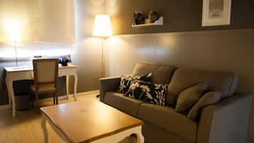 Una sala de estar con un sofá, una mesa de centro de madera, una lámpara, una silla y una mesita con lámpara.