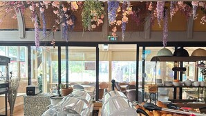 Un bufé de desayuno con diversos alimentos, un dispensador de jarabe de arce y flores decorativas colgantes.