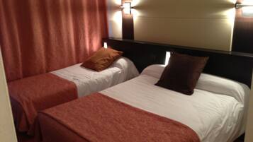 Ein Hotelzimmer mit zwei Einzelbetten, jedes mit einem braunen Kopfkissen und einer weißen Bettdecke. Über den Betten befindet sich ein großer Spiegel und an den Wänden sind Lampen angebracht.