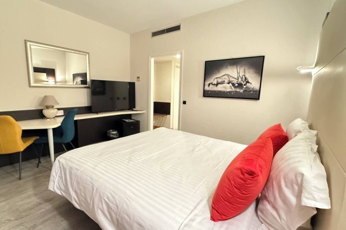 A hotel room with a bed, a desk, a chair, a television, and a picture on the wall.