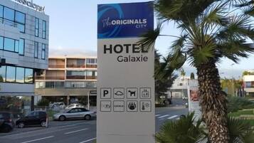 A hotel sign for 'The Originals City Hotel Galaxy' with amenities icons for parking, pool, pet-friendly, and other services.