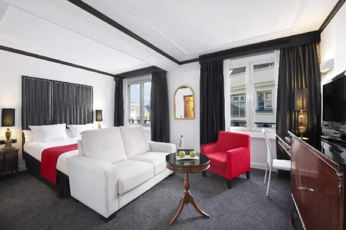Ein Hotelzimmer mit einem Bett, einem weißen Sofa, einem roten Sessel, einem kleinen runden Tisch und einem Fernseher.