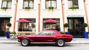 Un coche rojo antiguo estacionado frente a un edificio con terraza y plantas en macetas.