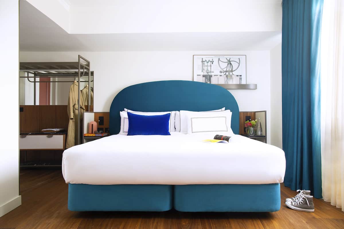Ein modernes Hotelzimmer mit einem großen Bett, einem Kleiderschrank, einem Schreibtisch und einem gerahmten Bild an der Wand.