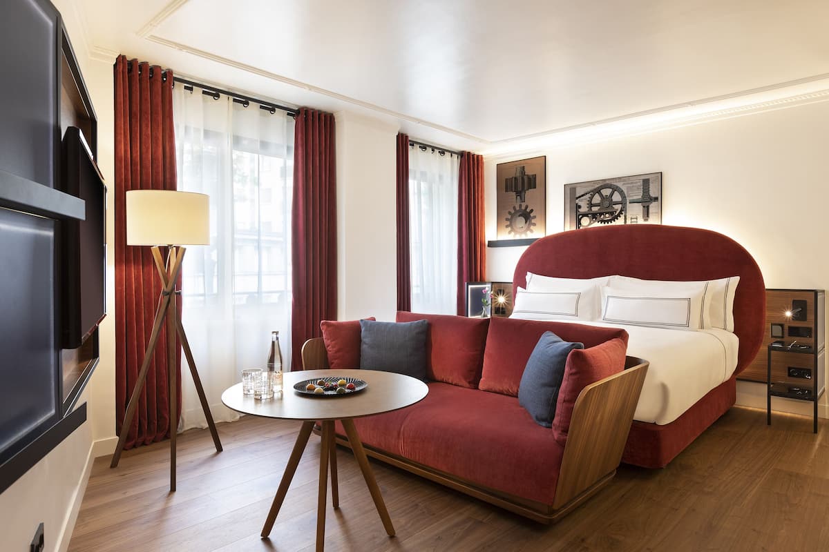 Ein Hotelzimmer mit einem großen Bett, einem roten Sofa, einem kleinen runden Tisch und einem Fernseher.