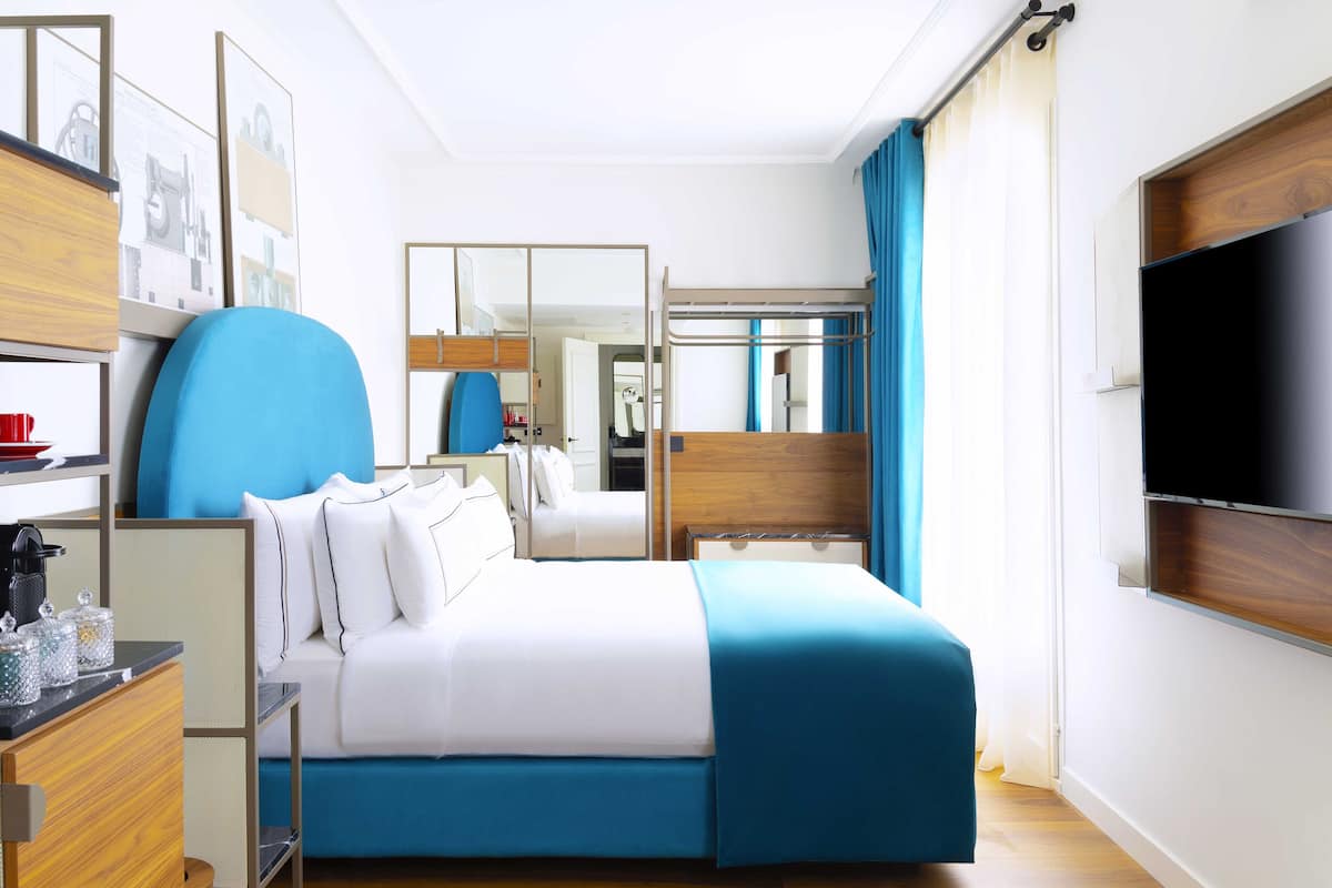 Ein modernes Hotelzimmer mit einem Bett, einem Schreibtisch, einem Sessel, einem Fernseher und einem Kleiderschrank.