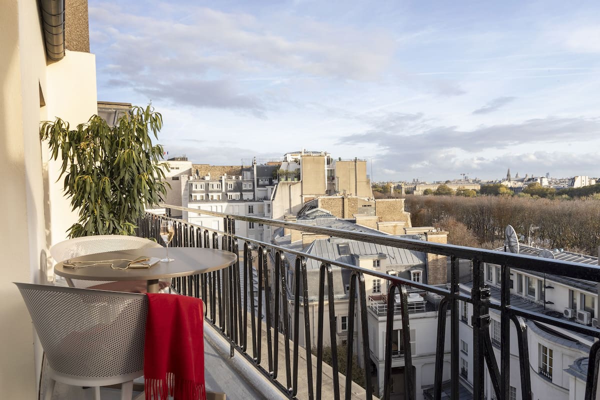 Ein Balkon mit Tisch und Stühlen, mit Blick auf eine Stadtlandschaft mit Gebäuden und blauem Himmel.