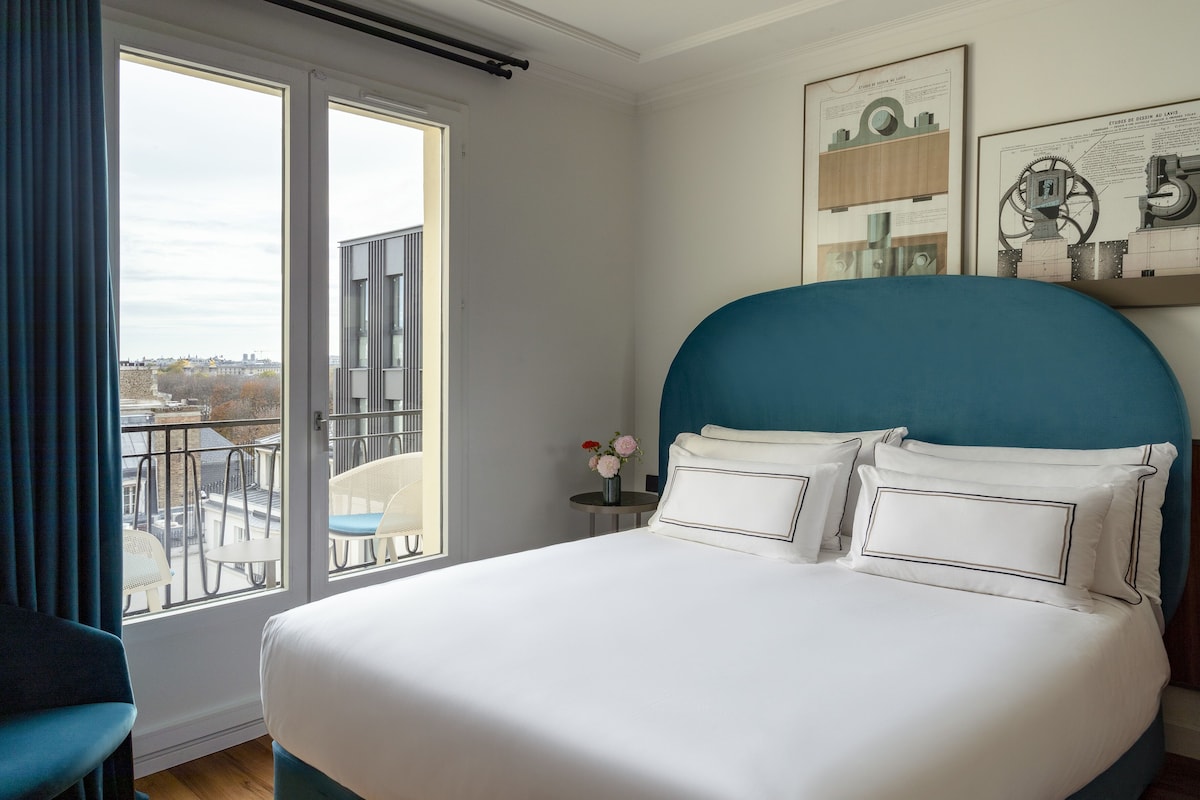 A hotel room with a large bed, a balcony with chairs, and a view of the city.