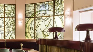 A bar area with a patterned carpet, bar stools, and a decorative wall with stained glass. - Hôtel Mercedes (Paris)