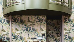 A room with a curved balcony, a wooden table, two chairs, and a floral wallpaper design. - Hôtel Mercedes (Paris)