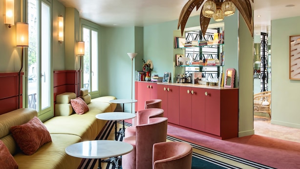 A cozy lounge area with a sofa, round tables, and a pink cabinet with books. - Hôtel Mercedes (Paris)