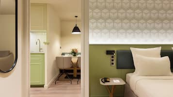 Ett hotellrum med en säng, ett litet bord, en stol, ett skrivbord och ett litet kök.