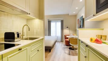 Une chambre d’hôtel compacte comprenant un coin cuisine, un lit, un petit espace repas et une fenêtre avec des rideaux.