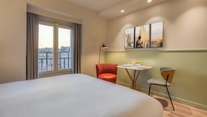 A hotel room with a large bed, a dining table with chairs, a city view through the window, and a painting on the wall. - Citadines Les Halles Paris (Paris)