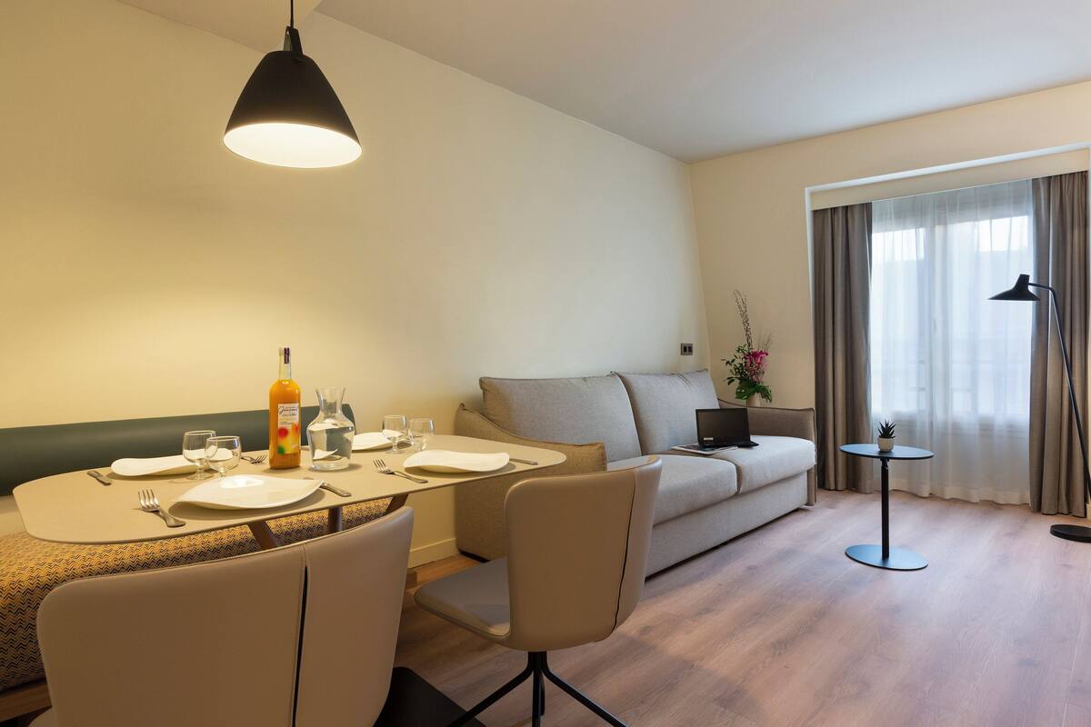 A modern living room with a dining area, a sofa, and a small table with a plant.