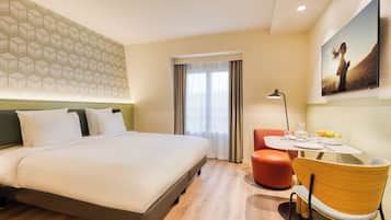 Una camera d'hotel con un letto, un tavolo da pranzo con sedie, una finestra con tende e una TV a parete.