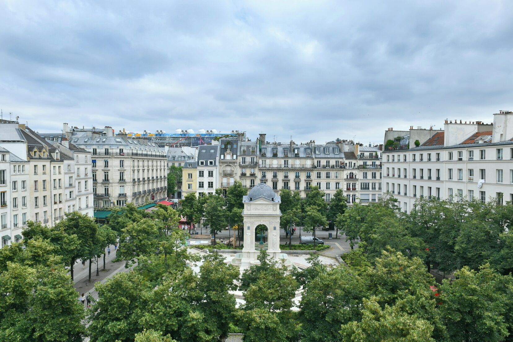 Une place historique, ornée d’un monument central, et bordée d’immeubles à étages dont les façades sont uniformes.