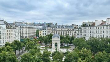 Uma praça histórica com um monumento central, rodeada por edifícios altos com fachadas uniformes.