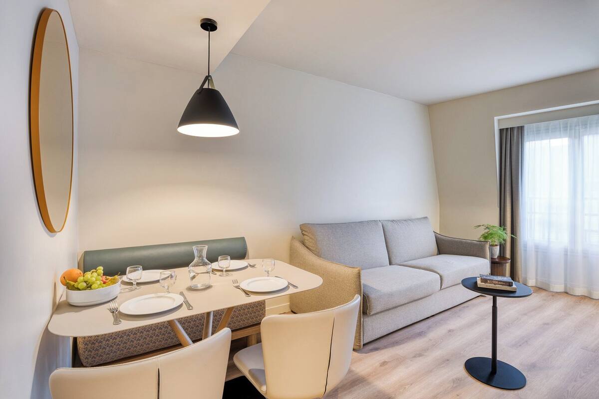 A modern living room with a dining area, a sofa, and a small table with a plant.