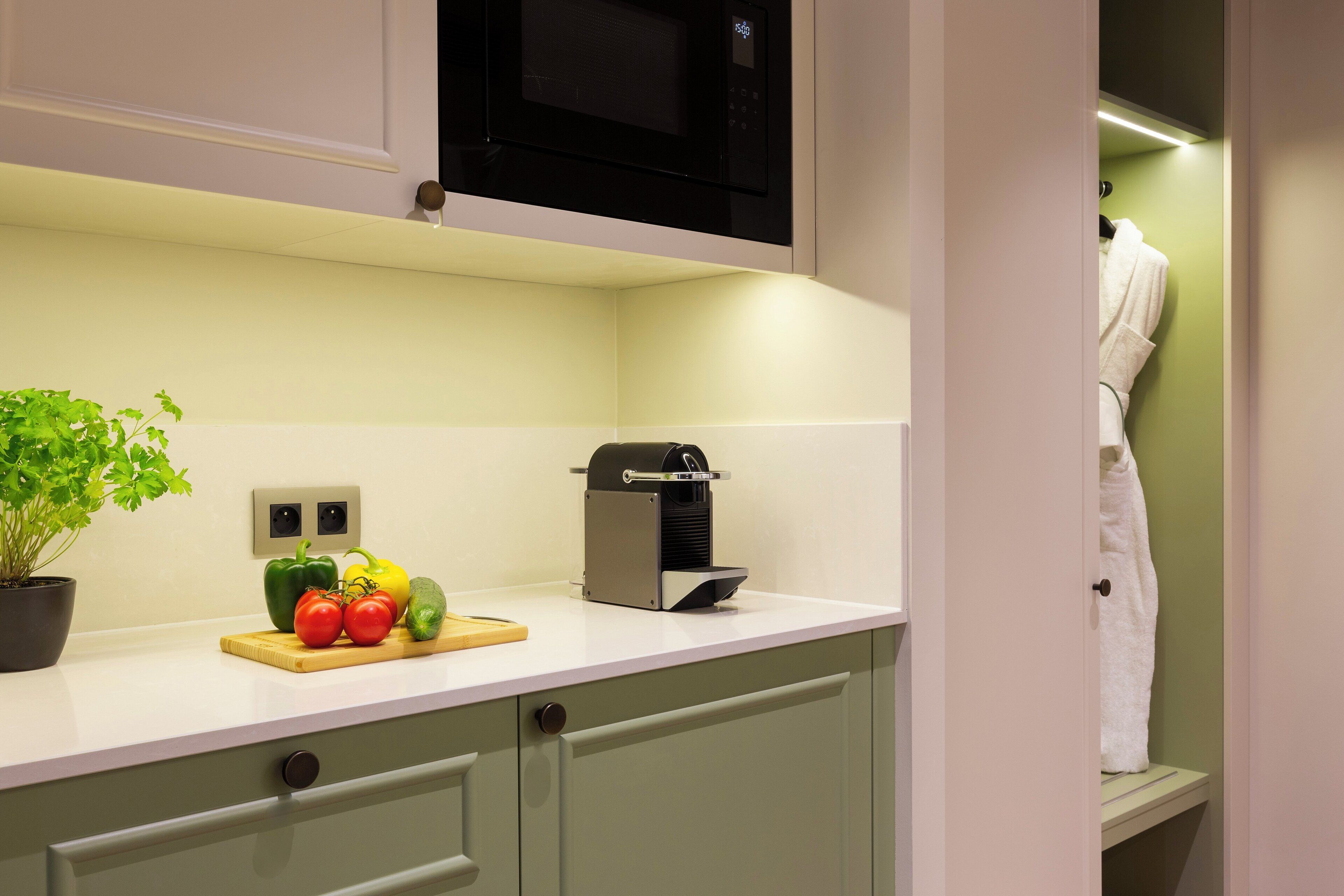 A kitchen with a microwave, a toaster, and a plant with vegetables on the counter.