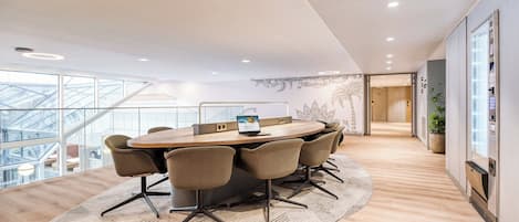 A modern conference room with a large oval table, six chairs, and a laptop.