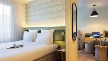 A hotel room with a bed, a desk with a laptop, a sofa, and a small table with a vase.