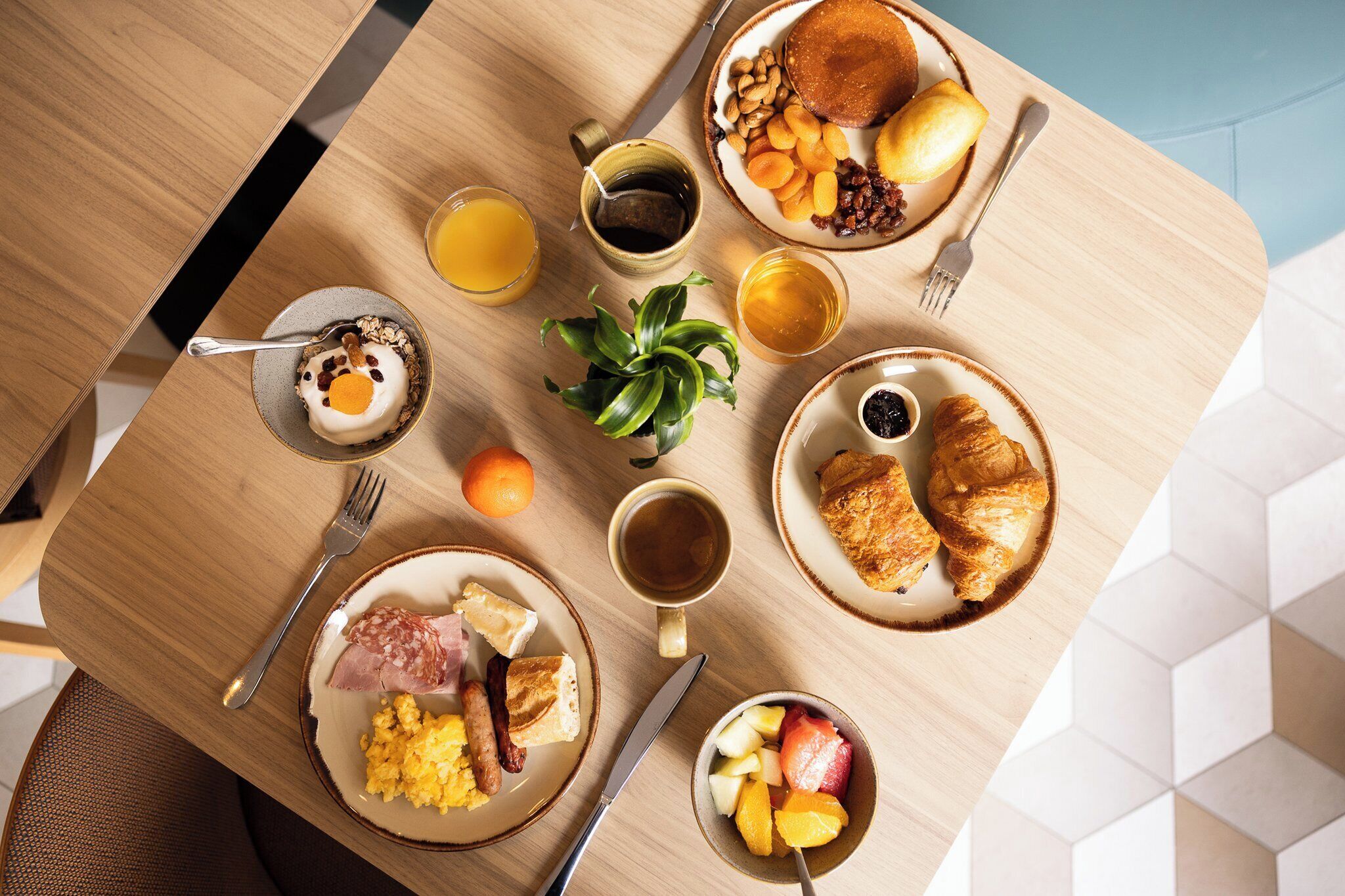 A breakfast table with plates of food, a coffee cup, a plant, and a fruit bowl.