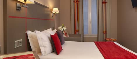 A hotel room with a bed, two wall-mounted lamps, a window with curtains, and a TV on the wall.