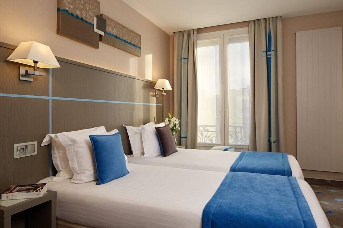 Ein Hotelzimmer mit zwei Betten, einem Nachttisch, einer Lampe, einem Fenster mit Vorhängen und einem Wandbild.