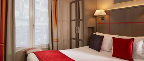 Habitación de hotel con una cama grande, una mesita de noche con lámpara, una ventana con cortinas y un cuadro en la pared.
