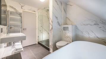 A modern bathroom with a marble wall, a toilet, a sink, and a shower area.