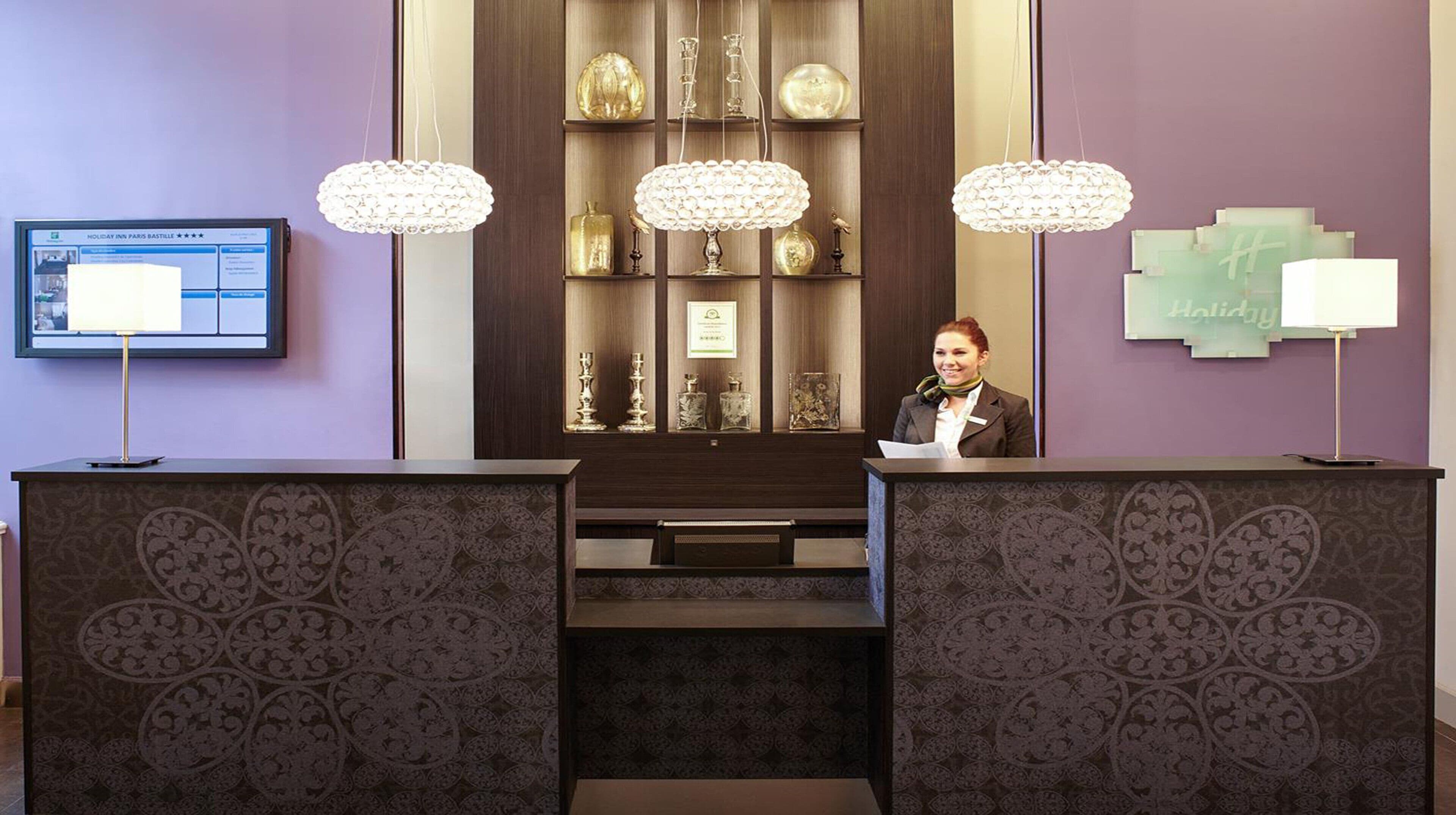 Un mostrador de recepción con una pantalla digital, una vitrina decorativa y una recepcionista.