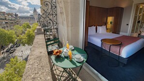 A hotel room with a bed, a small table with breakfast items, a view of the city, and a balcony with a chair and table. - Holiday Inn Paris - Gare de Lyon Bastille by IHG (Paris)