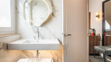 Un baño moderno con un lavabo de mármol, un espejo redondo y un banco.