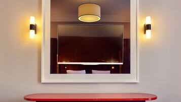 A framed mirror with a red table in front, two wall-mounted light fixtures, and a hanging light fixture above.
