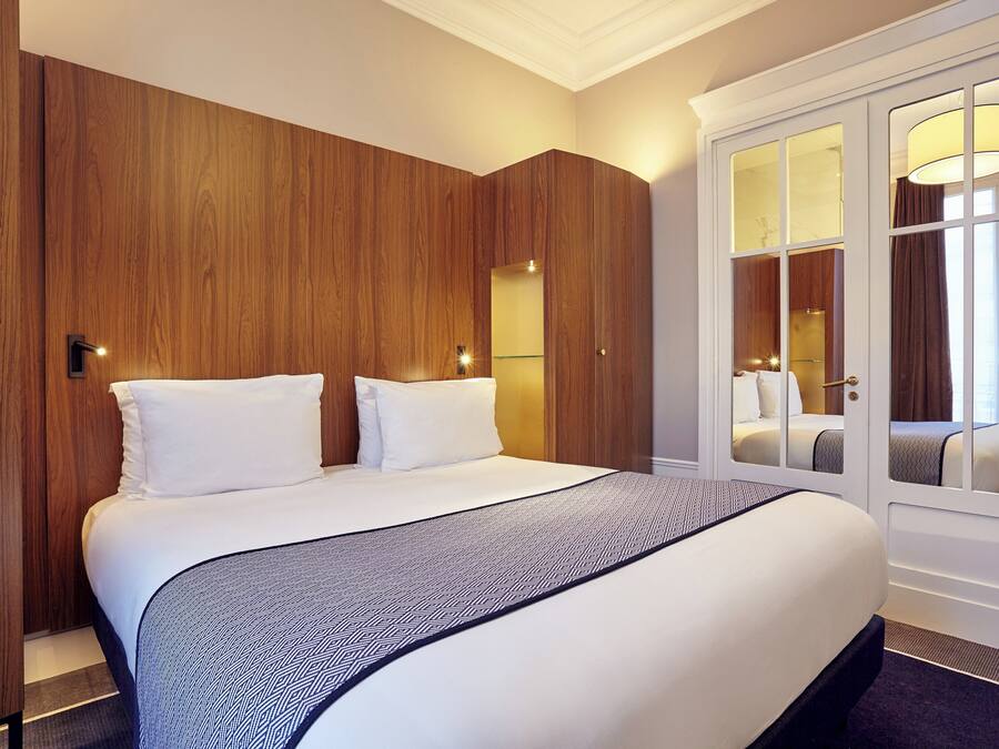 A hotel room with a large bed, wooden wardrobe, and a glass door leading to a balcony.