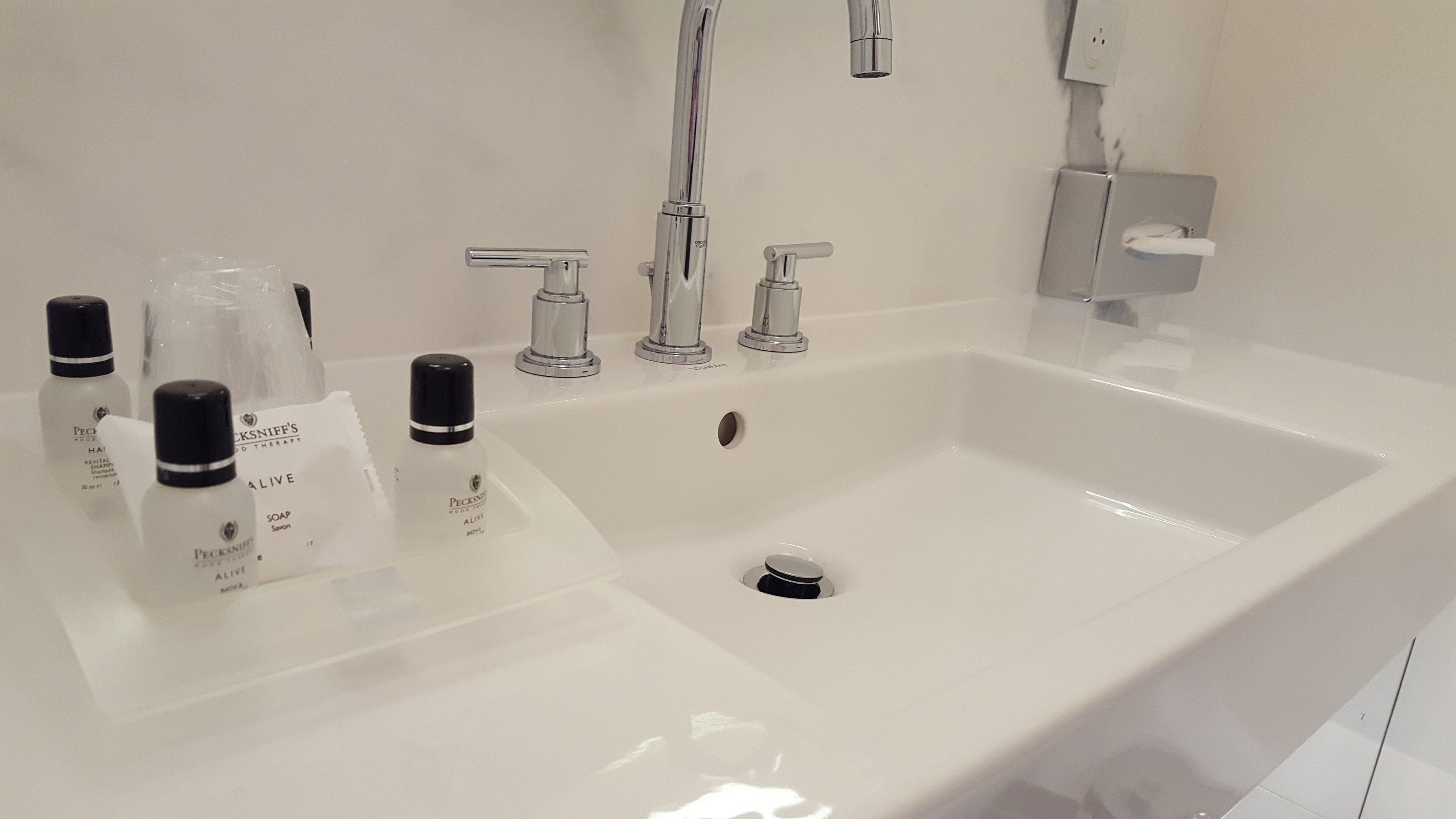 Un baño moderno con un lavamanos grande blanco, dos grifos y varios artículos de aseo.