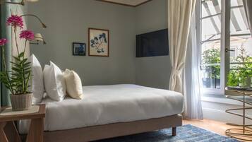 Une chambre à coucher avec un lit, une plante en pot, un tableau encadré et une fenêtre avec des rideaux.