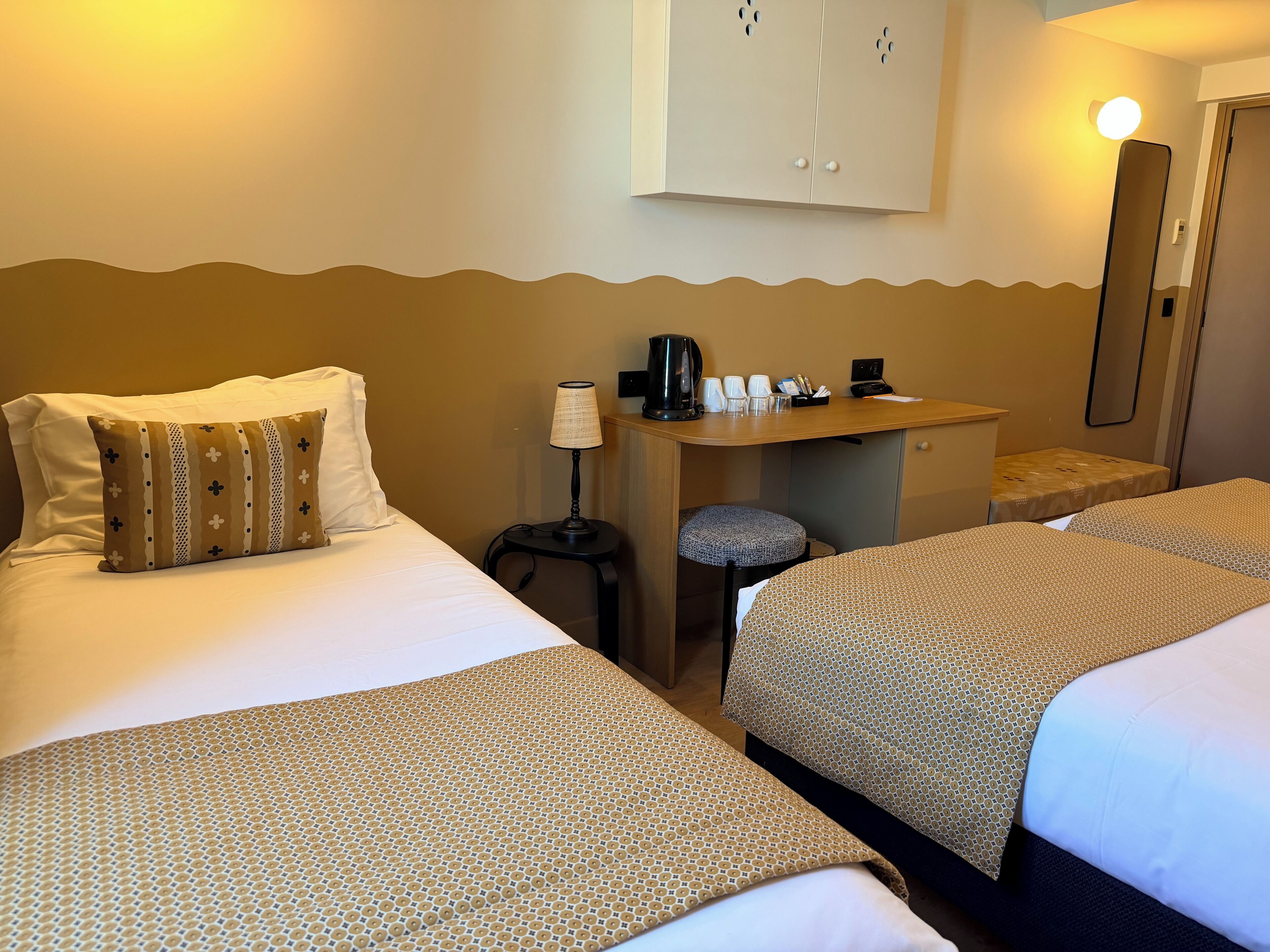 Une chambre d’hôtel avec deux lits, un bureau avec une lampe, une machine à café et un miroir.
