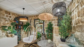 A cozy interior with a stone wall, wicker furniture, and a variety of plants. - Hotel Berne Opera (Paris)