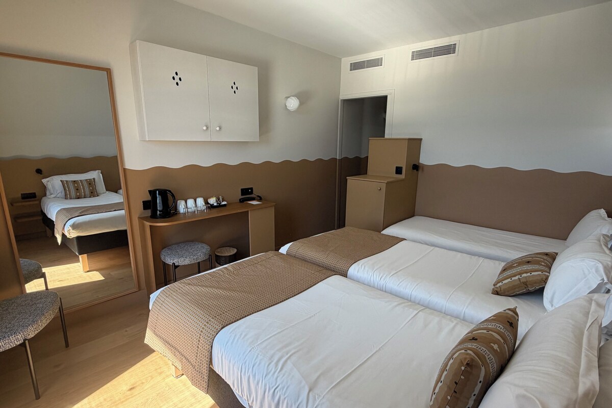 A hotel room with two beds, a desk, a chair, a wardrobe, and a mirror.