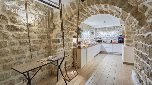 A rustic stone-walled kitchen with a wooden table and hanging ropes. - Hotel Berne Opera (Paris)