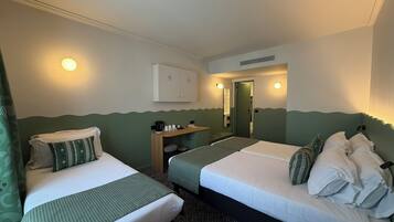 Hotellihuone, jossa on kaksi sänkyä, pieni työpöytä, peili ja ovi, joka johtaa kylpyhuoneeseen.