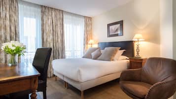A hotel room with a bed, a desk with a vase of flowers, a chair, and two bedside lamps.