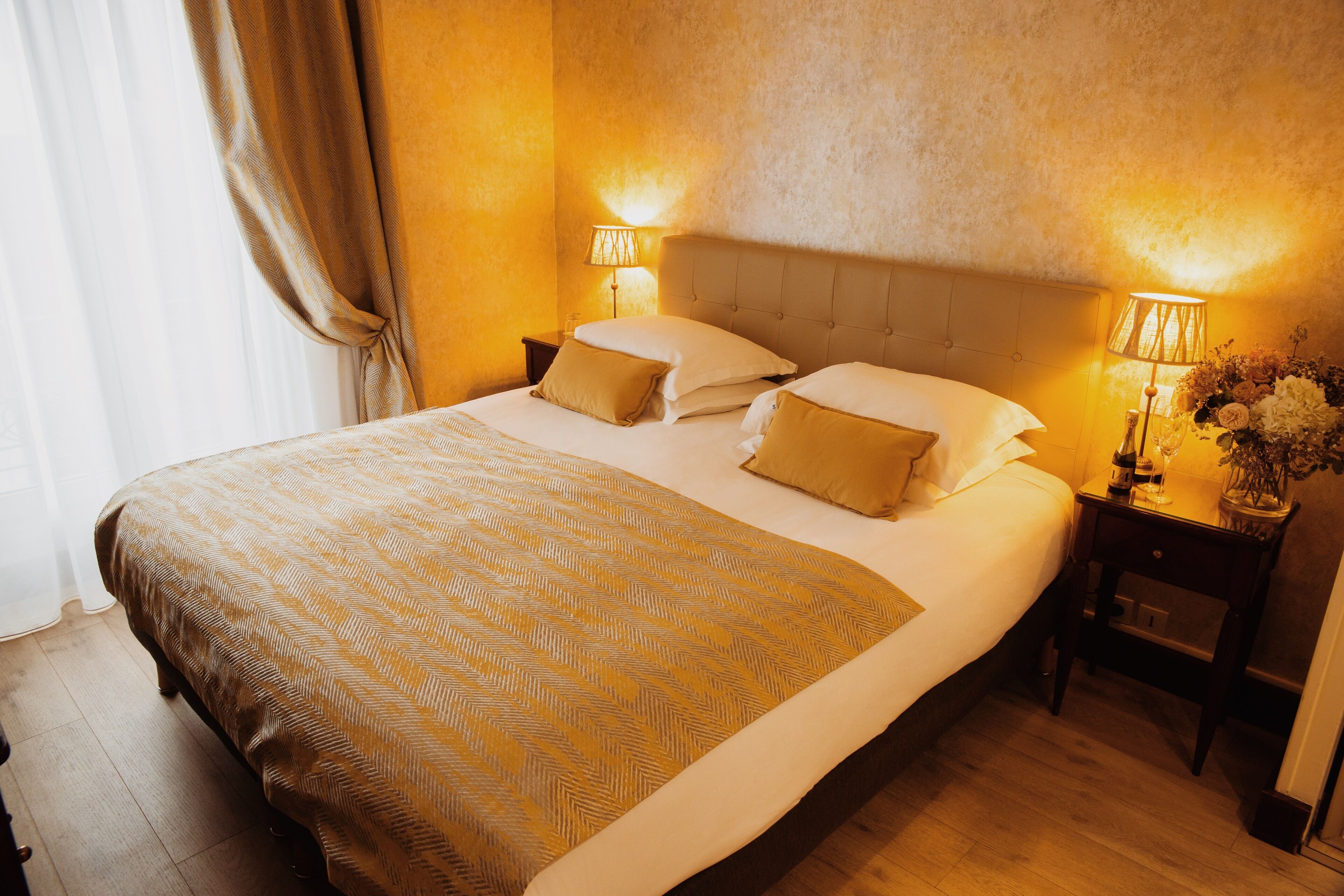 Ένα στρωμένο κρεβάτι με προσεγμένο τρόπο, με ένα διακοσμητικό κάλυμμα, δύο φωτιστικά κομοδίνου και ένα κομοδίνο με ένα βάζο γεμάτο λουλούδια.