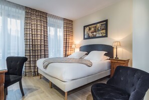 Una habitación de hotel con una cama, dos sillas, una mesita de noche y una lámpara.