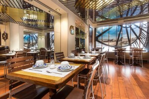 Un restaurante con mesas y sillas de madera, un diseño de techo moderno y amplios ventanales que ofrecen vistas de la ciudad.