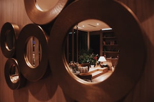 Una ventana circular que muestra un salón, con un sofá, una lámpara y plantas en macetas.